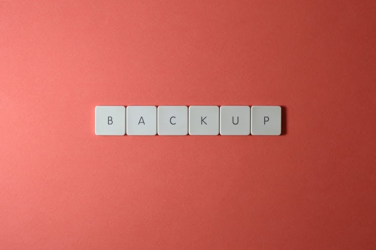 Close-up of keyboard keys spelling 'BACKUP' placed on a coral-colored surface.