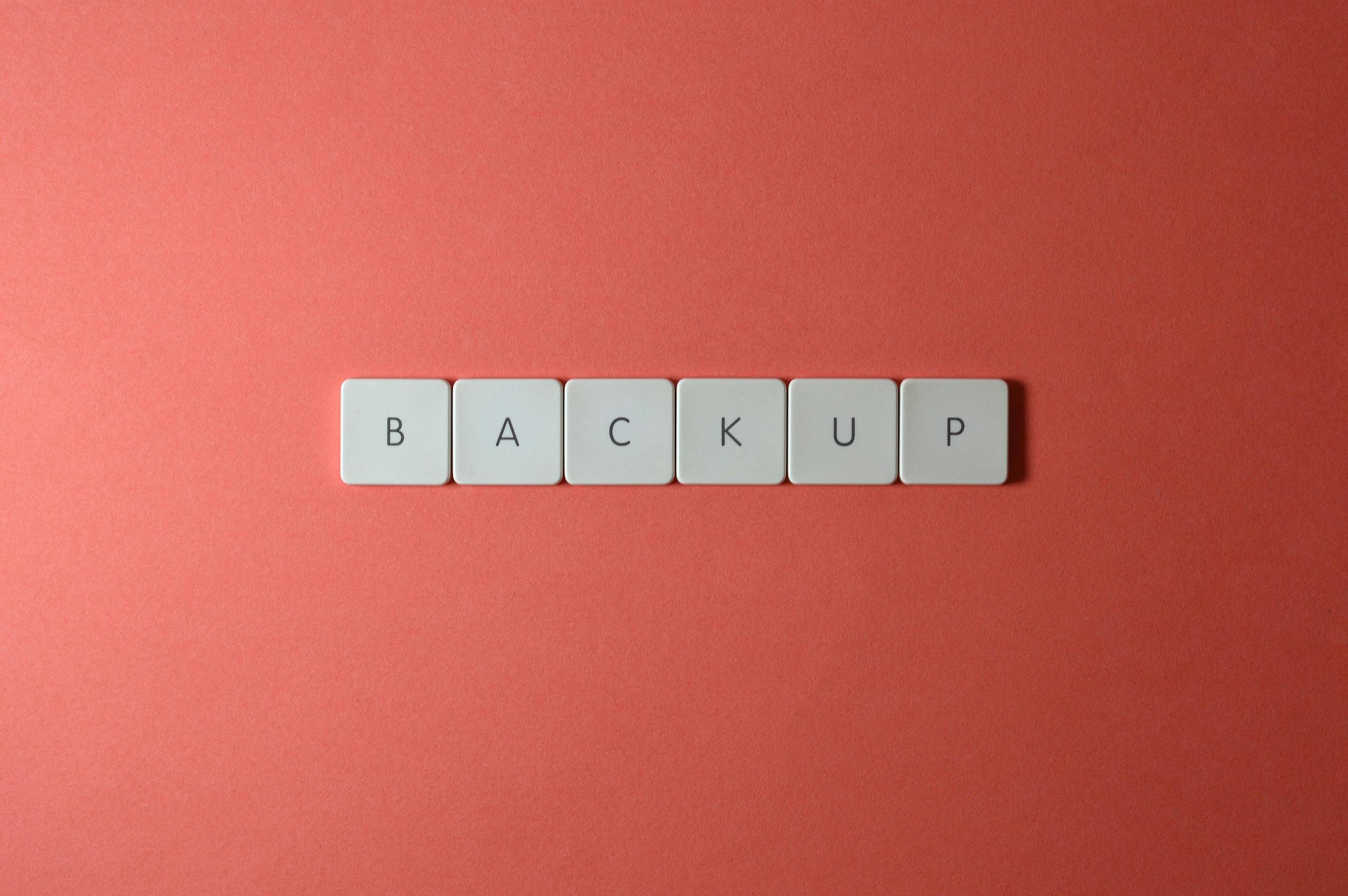 Close-up of keyboard keys spelling 'BACKUP' placed on a coral-colored surface.